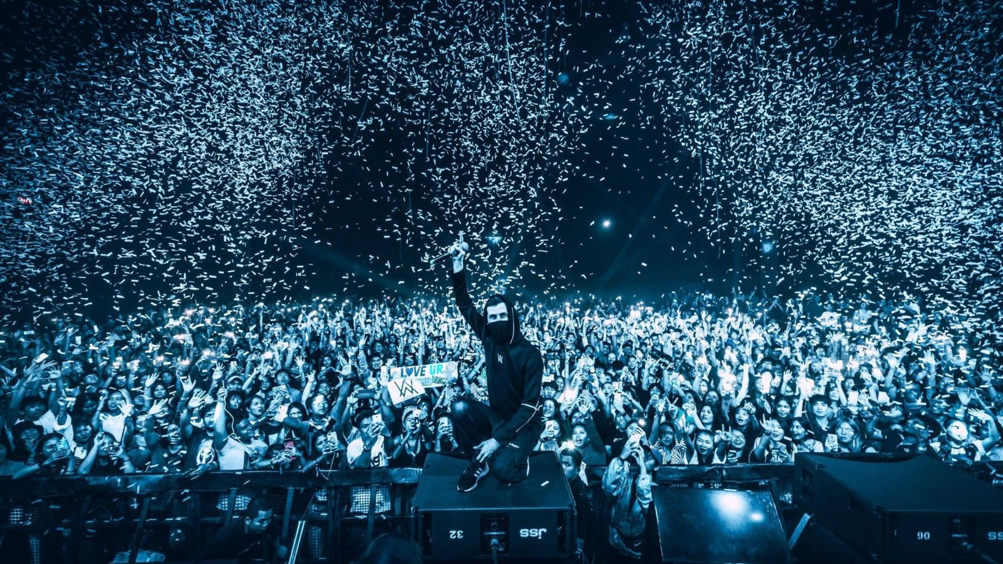 Alan Walker posing in front of a large crowd during a live performance as confetti falls around the venue