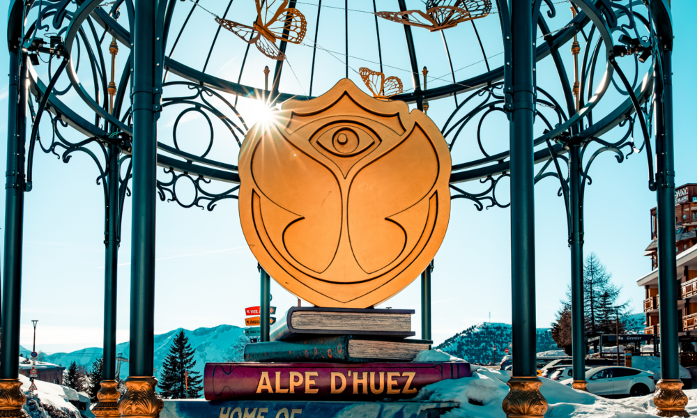 Tomorrowland logo displayed in Alpe d’Huez with snowy mountains and resort buildings in the background