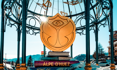 Tomorrowland logo displayed in Alpe d’Huez with snowy mountains and resort buildings in the background