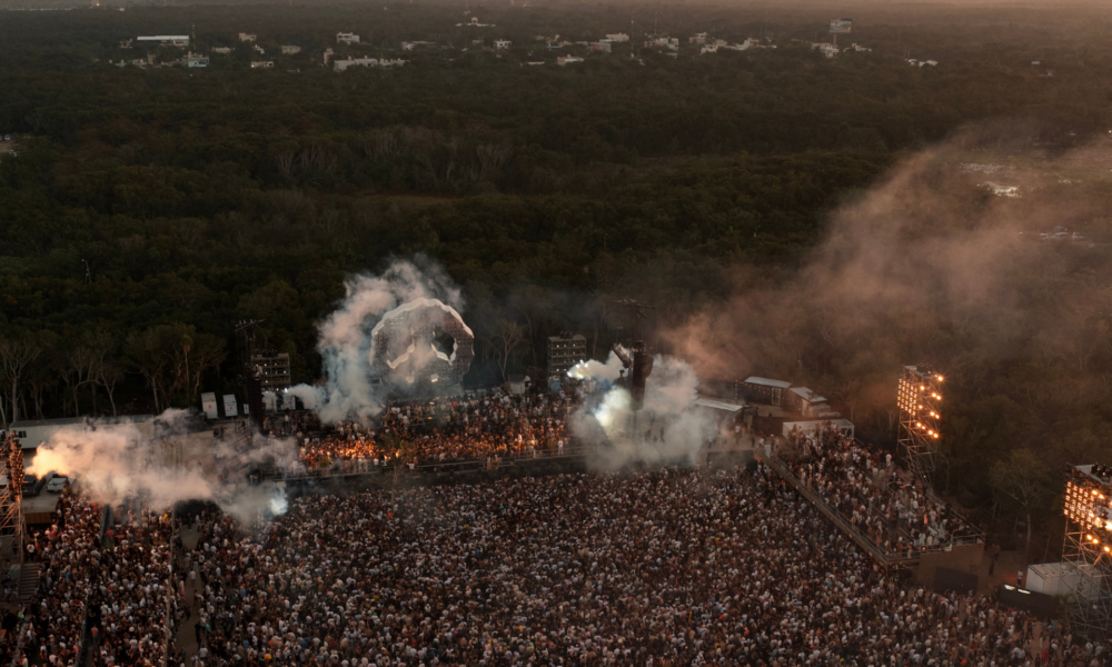 Aerial view of Zamna Tulum surrounded by jungle, with a large crowd, stage production, smoke and lighting at sunset