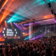 A DJ performs at Asia Music Event in Hong Kong as a large crowd gathers in front of the stage with the Asia Music Event logo on screen.