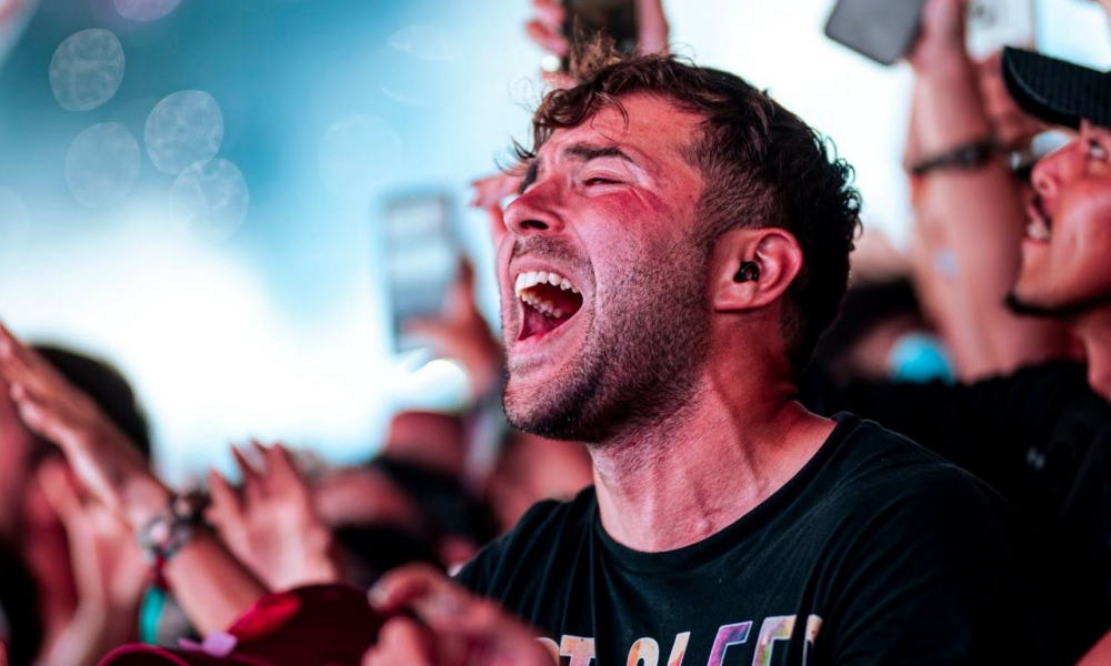 Festival attendee singing along with eyes closed and mouth open, surrounded by a cheering crowd and phones raised in the air