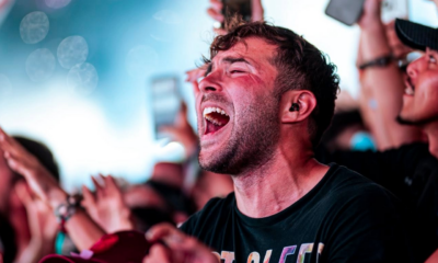 Festival attendee singing along with eyes closed and mouth open, surrounded by a cheering crowd and phones raised in the air