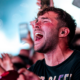 Festival attendee singing along with eyes closed and mouth open, surrounded by a cheering crowd and phones raised in the air