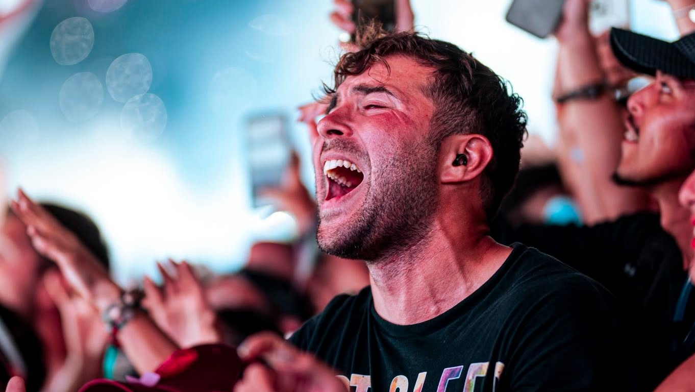Festival attendee singing along with eyes closed and mouth open, surrounded by a cheering crowd and phones raised in the air