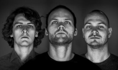 Black and white portrait of the three members of Noisia looking directly at the camera against a dark backdrop