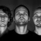 Black and white portrait of the three members of Noisia looking directly at the camera against a dark backdrop