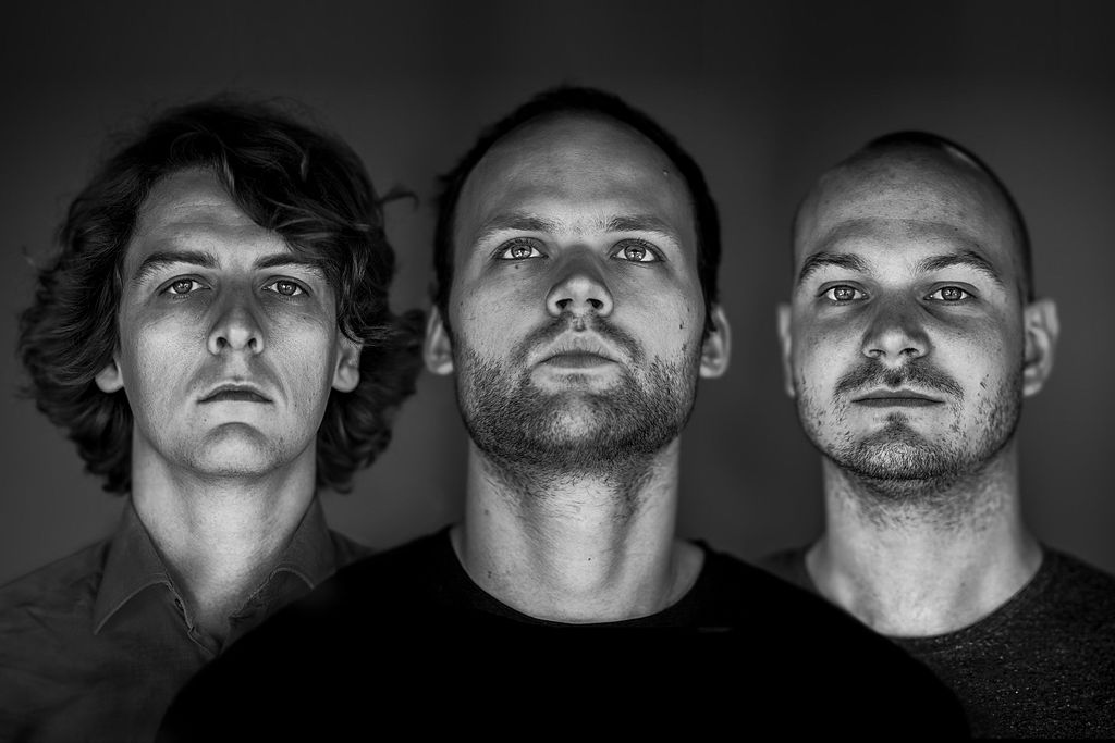 Black and white portrait of the three members of Noisia looking directly at the camera against a dark backdrop
