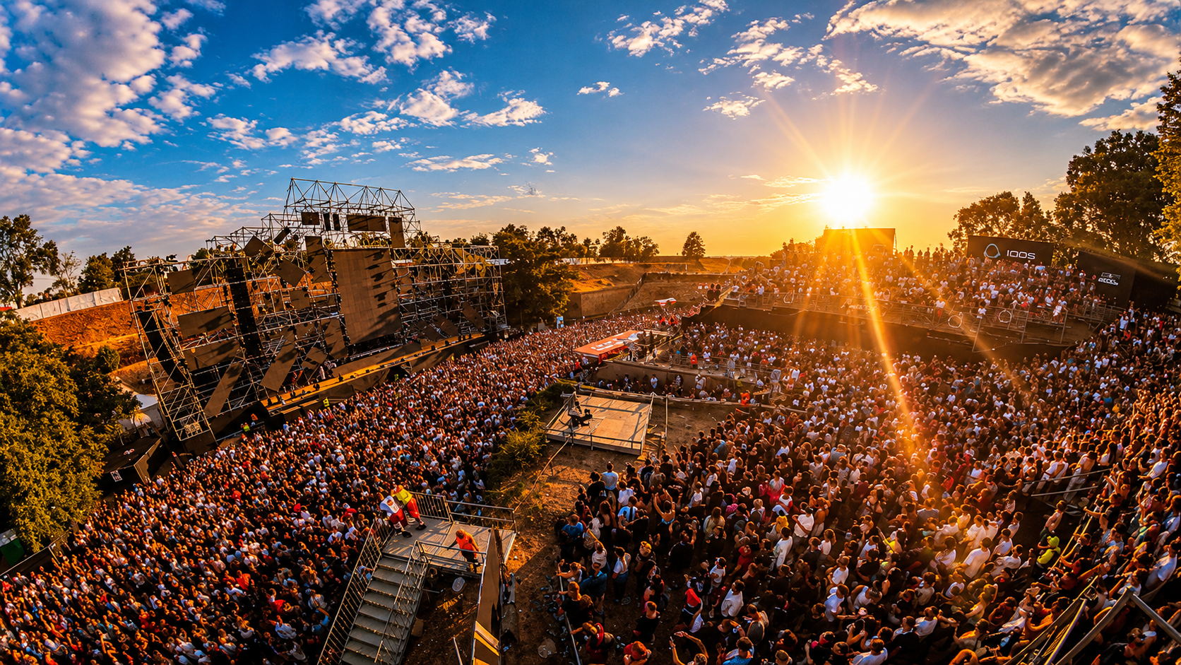 A large crowd gathers in front of a stage at EXIT Festival in Serbia during a sunset performance.