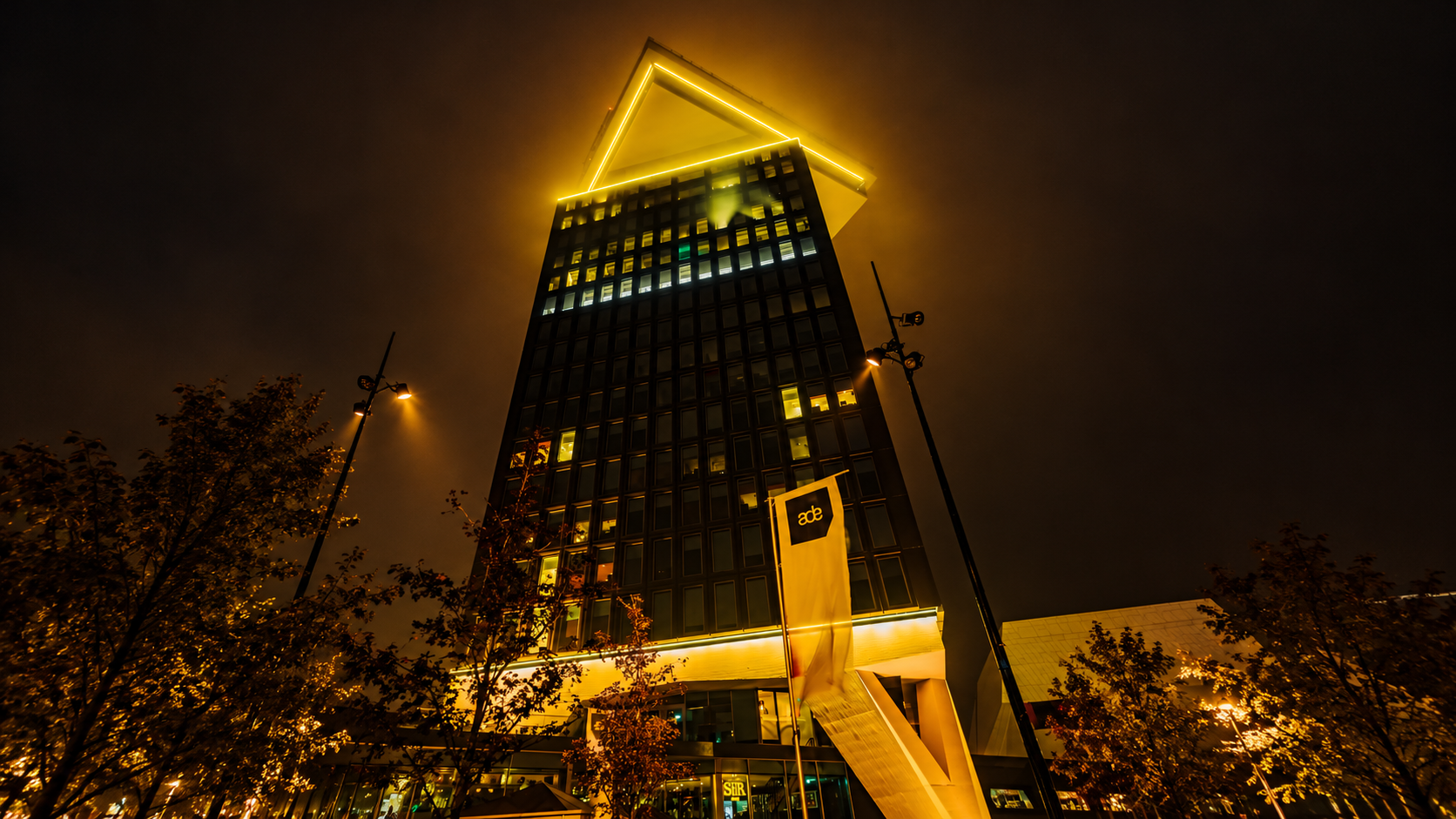 Amsterdam Dance Event branding illuminated in golden light on a high-rise building at night.