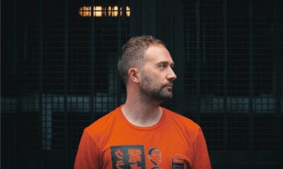 Scarper in an orange graphic T-shirt looking to the side in front of a dark metal grille