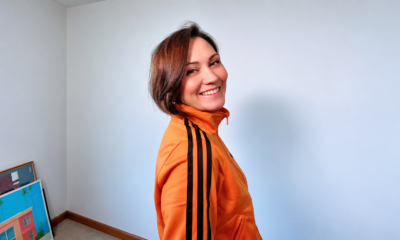 Edele Andaya smiling over her shoulder in an orange track jacket against a white wall
