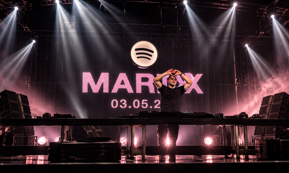 Martin Garrix makes a heart gesture during a performance beneath a Spotify logo and Marty album announcement backdrop.