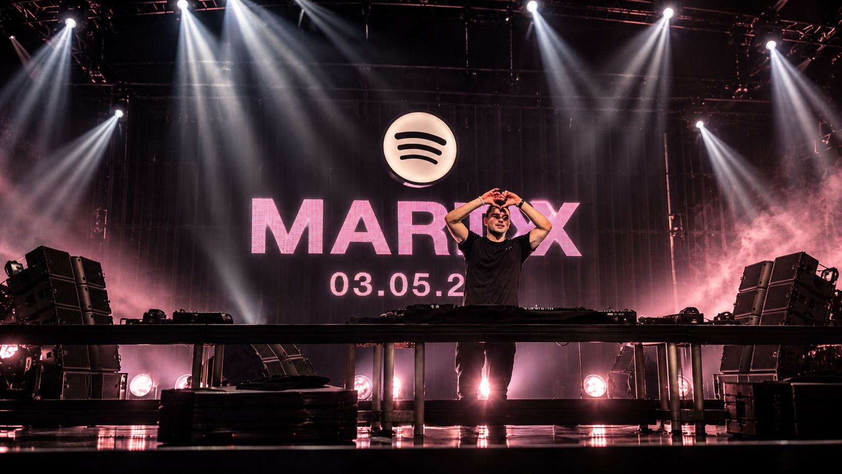 Martin Garrix makes a heart gesture during a performance beneath a Spotify logo and Marty album announcement backdrop.