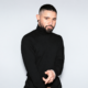 Skrillex wearing a black turtleneck in a studio portrait.