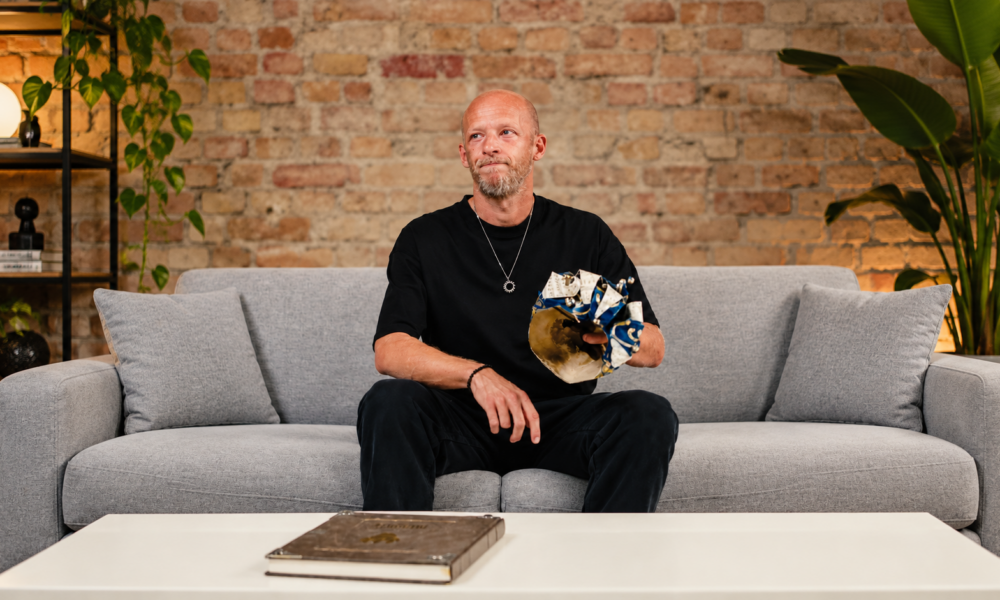 High-Tech Minimal DJ Boris Brejcha sits on a sofa holding his distinctive Joker mask during an announcement about his retirement and final tour.