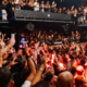 A crowded dancefloor at Amnesia Ibiza during the Metamorfosi 2026 closing, with the DJ booth surrounded by attendees under red lighting.