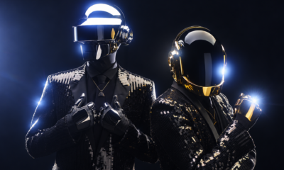 Daft Punk wearing their robot helmets and black sequined suits in a promotional photo