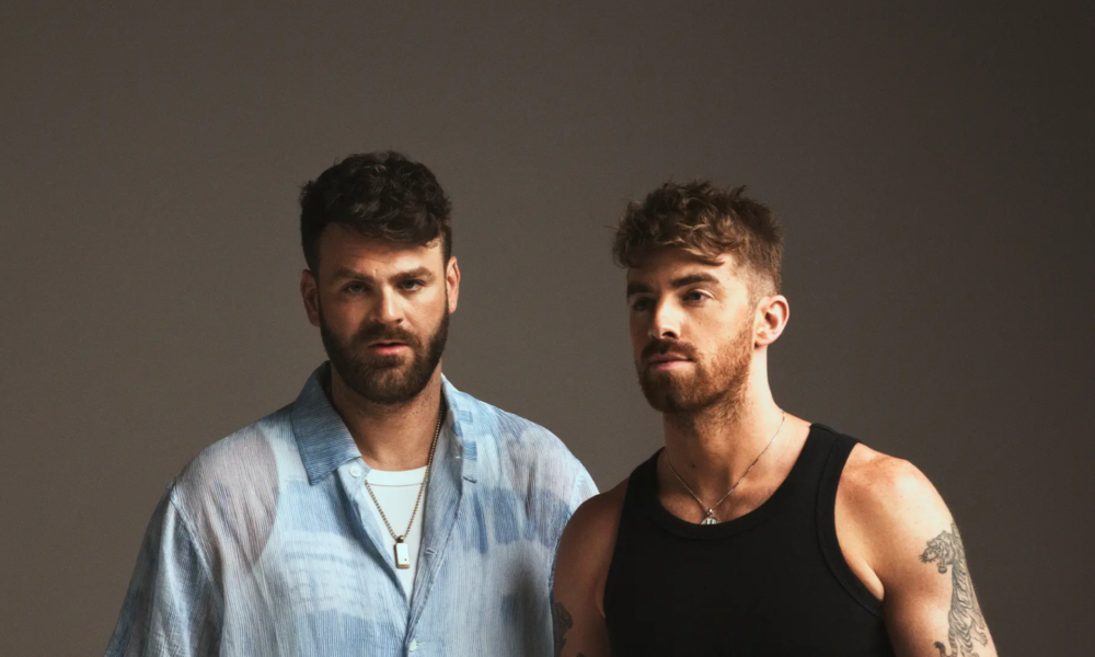 Promotional portrait for The Chainsmokers showing Alex and Drew posing against a dark studio background