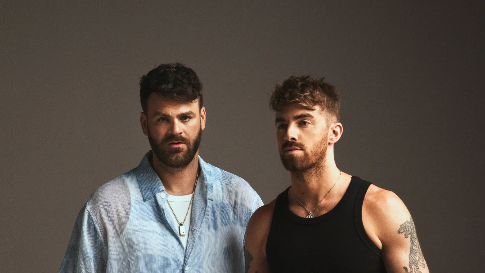 Promotional portrait for The Chainsmokers showing Alex and Drew posing against a dark studio background
