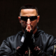DJ Snake wearing black sunglasses and a black jacket with his hands together