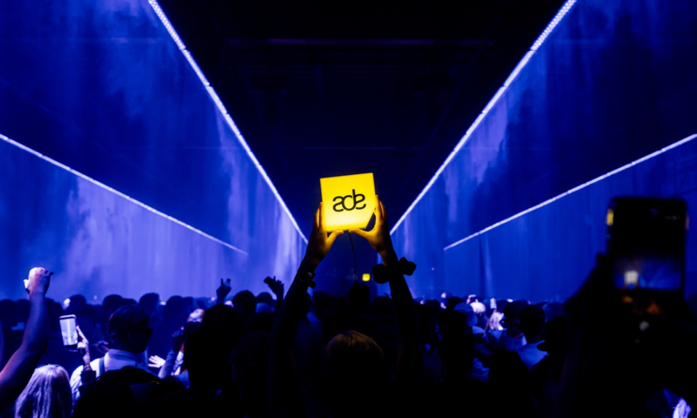 Crowd at Amsterdam Dance Event holding an illuminated ADE sign during a live electronic music event