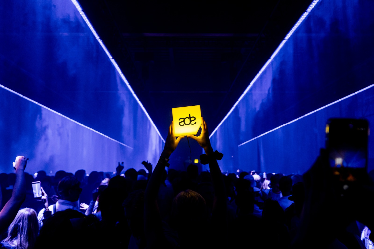 Crowd at Amsterdam Dance Event holding an illuminated ADE sign during a live electronic music event