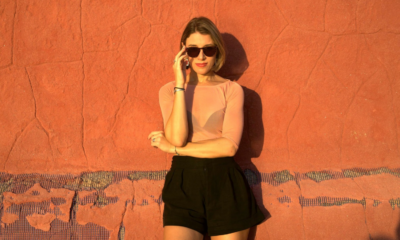 Ella Romand standing against an orange wall wearing sunglasses during a promotional shoot for her ‘More Love’ remix
