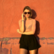 Ella Romand standing against an orange wall wearing sunglasses during a promotional shoot for her ‘More Love’ remix