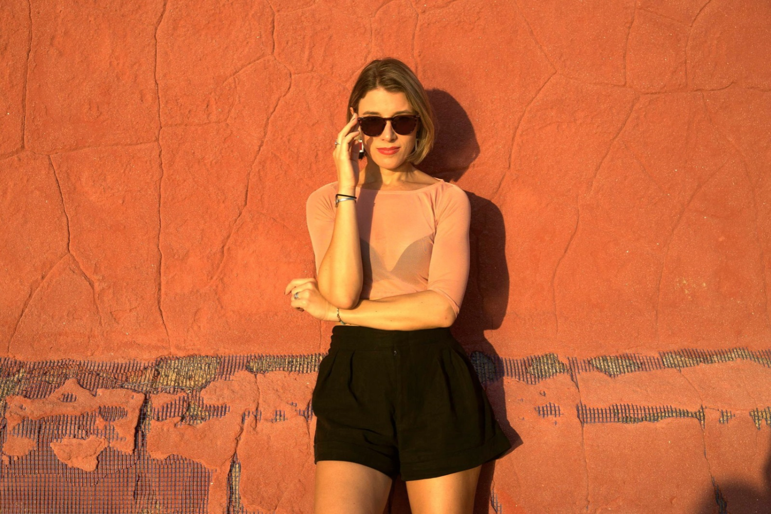 Ella Romand standing against an orange wall wearing sunglasses during a promotional shoot for her ‘More Love’ remix