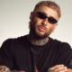 Lance Savali wearing black sunglasses and a black shirt in a promotional portrait for ‘All I See’