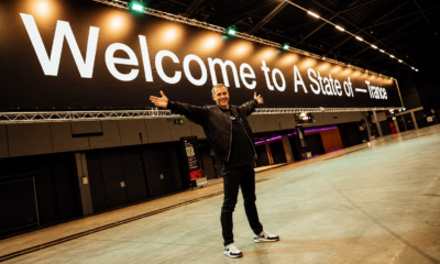 Armin van Buuren standing beneath a large “Welcome to A State of Trance” sign inside an event venue