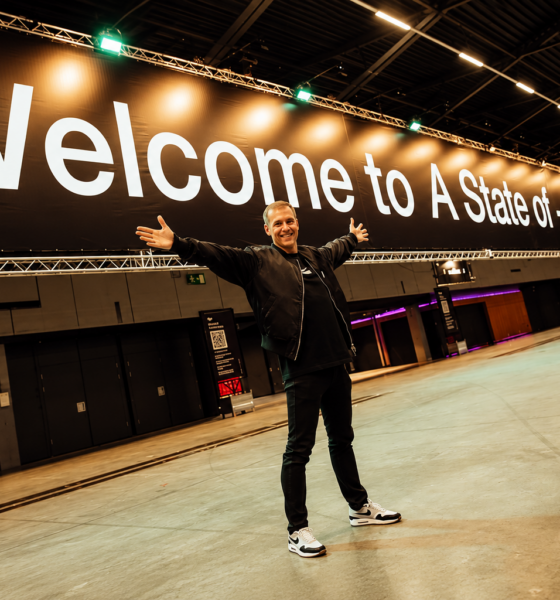 Armin van Buuren standing beneath a large “Welcome to A State of Trance” sign inside an event venue