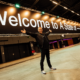 Armin van Buuren standing beneath a large “Welcome to A State of Trance” sign inside an event venue