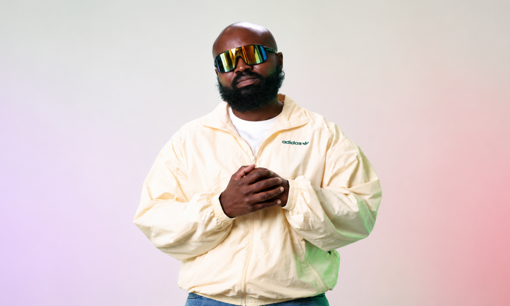 Audio Paak wearing reflective sunglasses and a cream Adidas jacket in a studio portrait