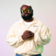 Audio Paak wearing reflective sunglasses and a cream Adidas jacket in a studio portrait