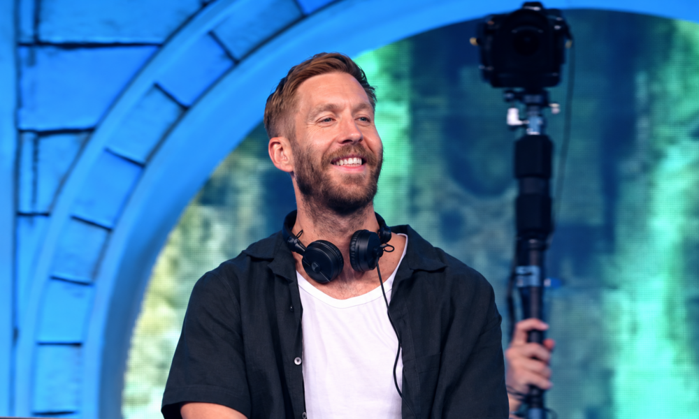 Calvin Harris smiling on stage with headphones around his neck during the 18 Months anniversary article