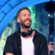 Calvin Harris smiling on stage with headphones around his neck during the 18 Months anniversary article