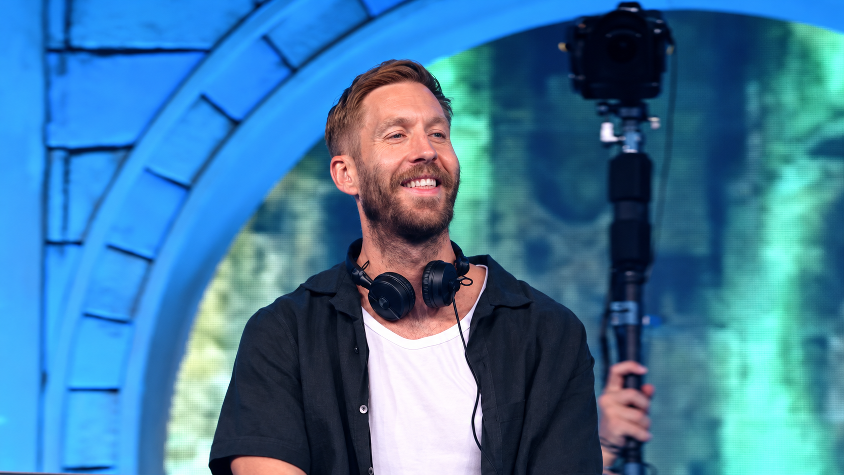 Calvin Harris smiling on stage with headphones around his neck during the 18 Months anniversary article