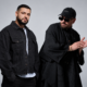 GROSSOMODDO and MOSKA posing together in black outfits against a light grey studio background