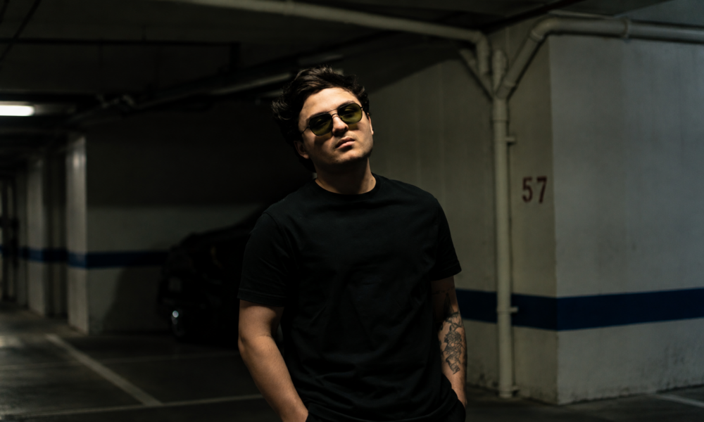 Nico Falla wearing dark clothing and blue sunglasses in a promotional portrait for his electronic music releases. Copy image title Copy alt text