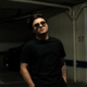 Nico Falla wearing dark clothing and blue sunglasses in a promotional portrait for his electronic music releases. Copy image title Copy alt text