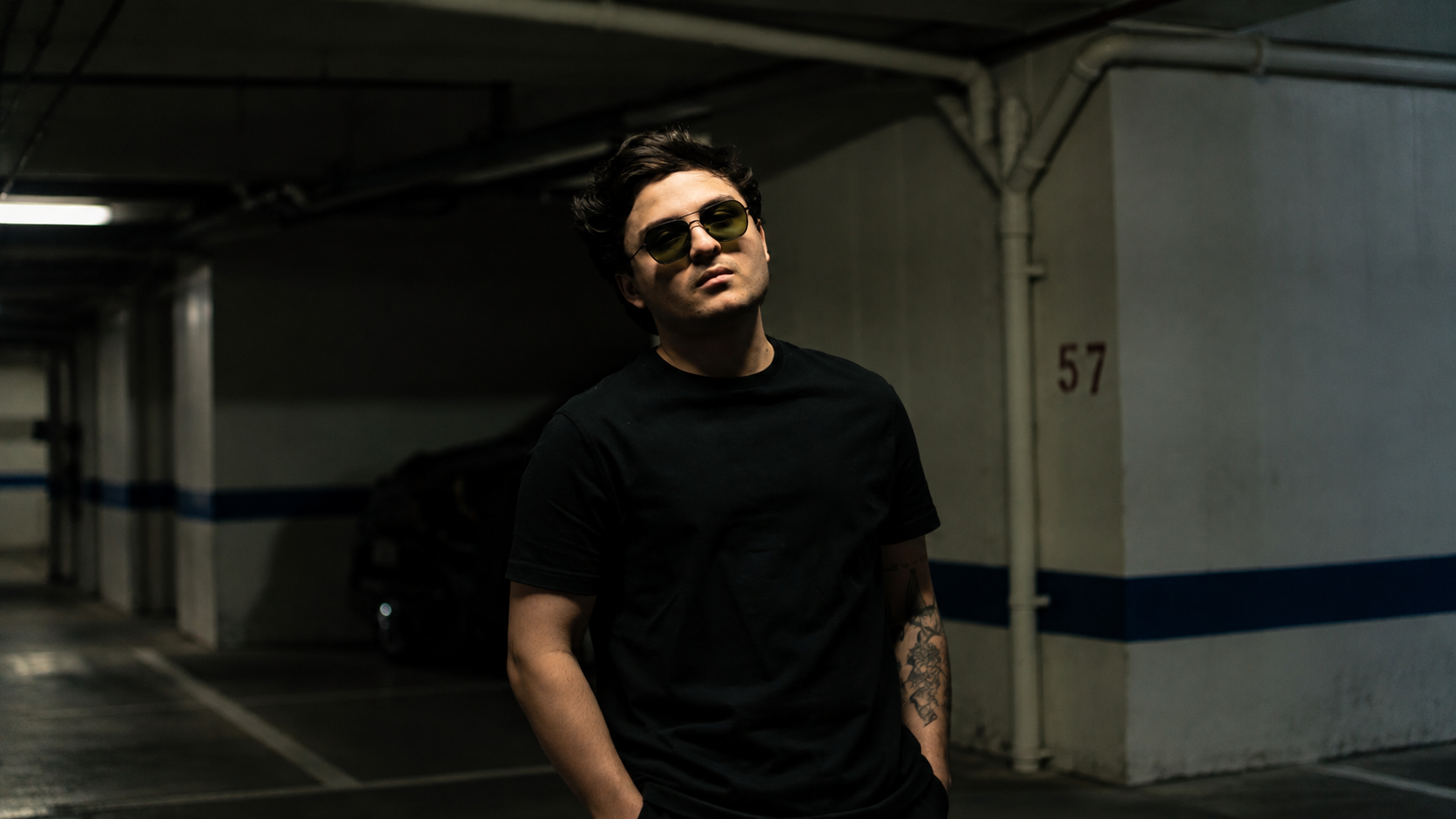 Nico Falla wearing dark clothing and blue sunglasses in a promotional portrait for his electronic music releases. Copy image title Copy alt text