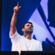Fred again.. performing on stage with one arm raised in front of a blue screen