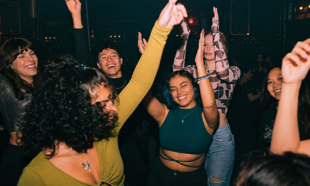 Young people dancing together inside a nightclub with their hands raised