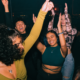 Young people dancing together inside a nightclub with their hands raised