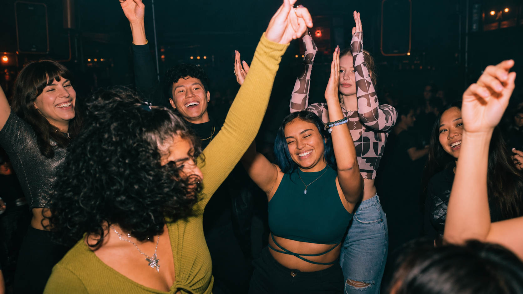 Young people dancing together inside a nightclub with their hands raised