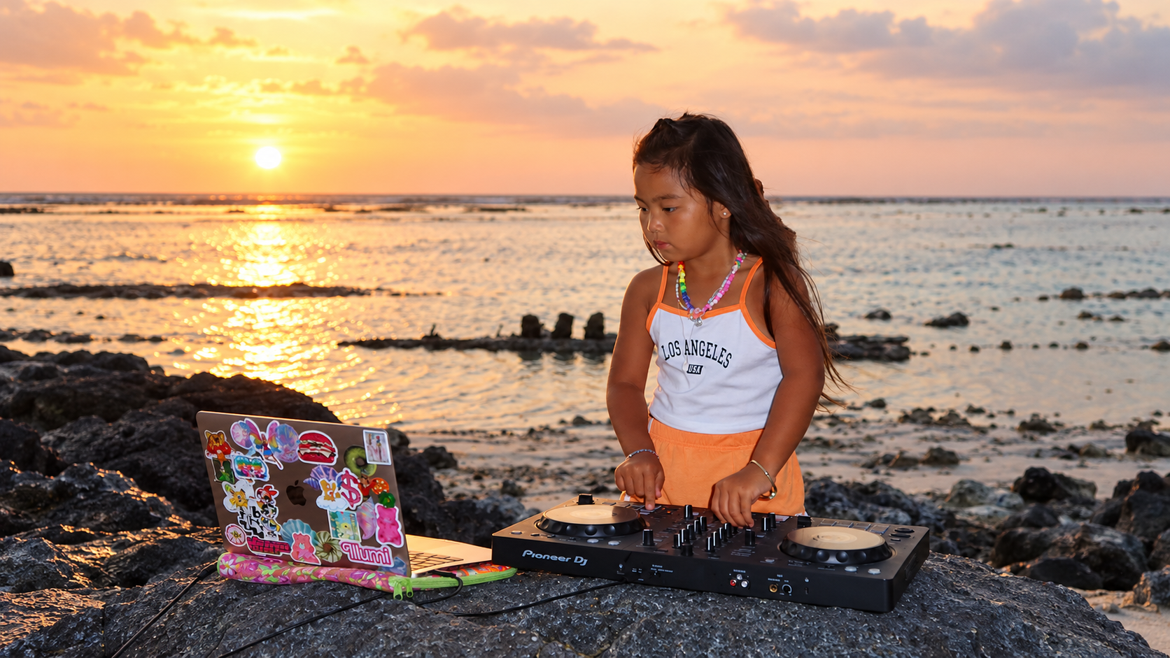 DJ ILLU using a Pioneer DJ controller beside the ocean at sunset