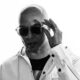 Black-and-white portrait of American house music DJ and producer Cevin Fisher wearing sunglasses and a white jacket.