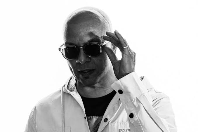 Black-and-white portrait of American house music DJ and producer Cevin Fisher wearing sunglasses and a white jacket.